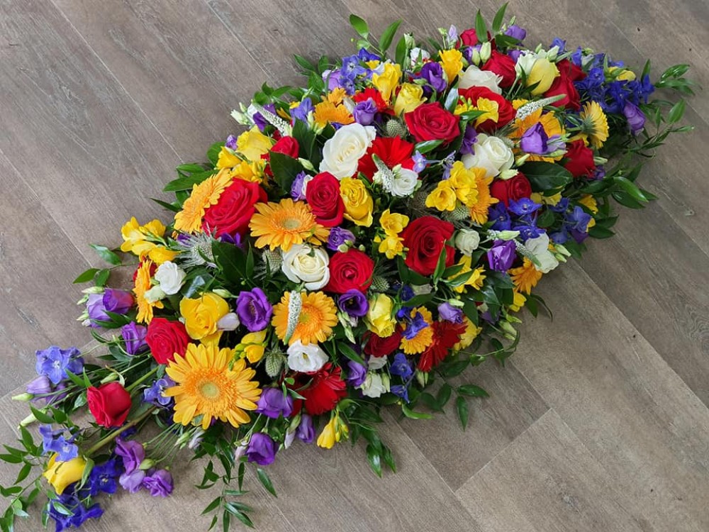 vibrant casket spray with yellow, red and purple