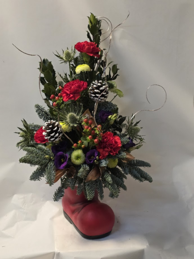 Santa's boot arrangement - Christmas gift arrangement wiin a lovely keepsake ceremic container, front facing arrangement, tradional colours with seasonal foliage and cones