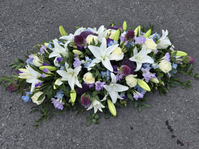 summery casket blue, lilac, purple - featuring a harmonious blend of whites, purples, and greens. Perfect for expressing heartfelt sentiments, this casket spray from Six Ways Florist in Llanelli adds a touch of grace in rememberance